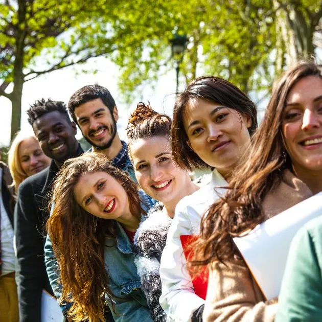 A diverse group of students standing in a line outdoors, smiling and holding books, symbolizing collaboration and cultural exchange during study tours.
