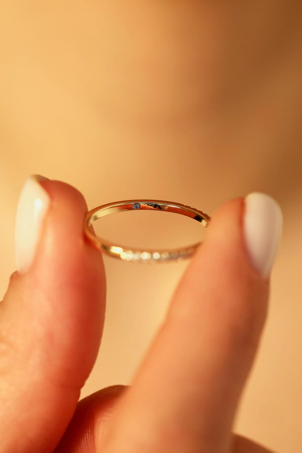 Yellow gold diamond band with a hidden birthstone set inside the ring, held between two fingers, from Nangi.