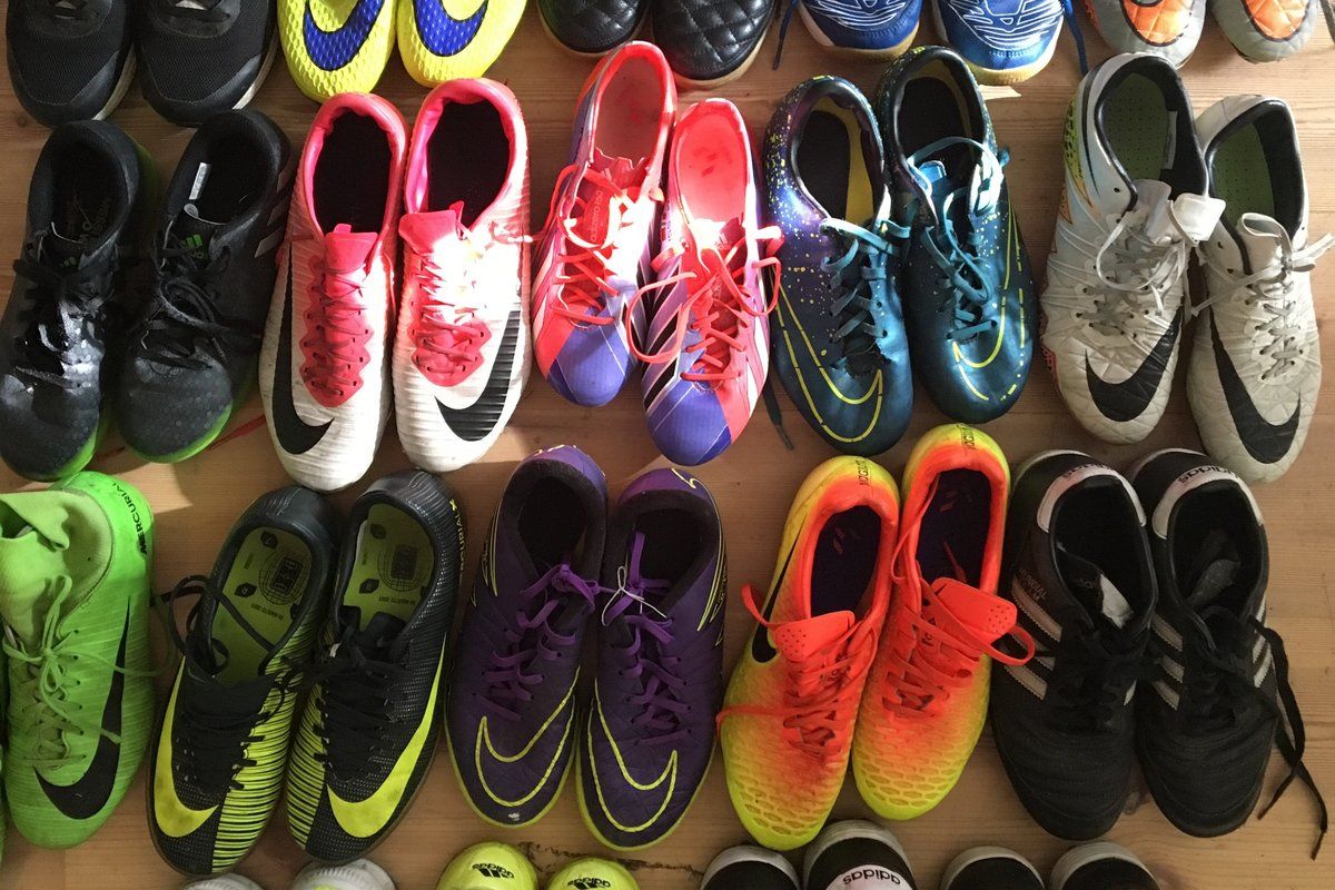 Brukte fotballsko i mange farger satt på rekke og rad på et tregulv