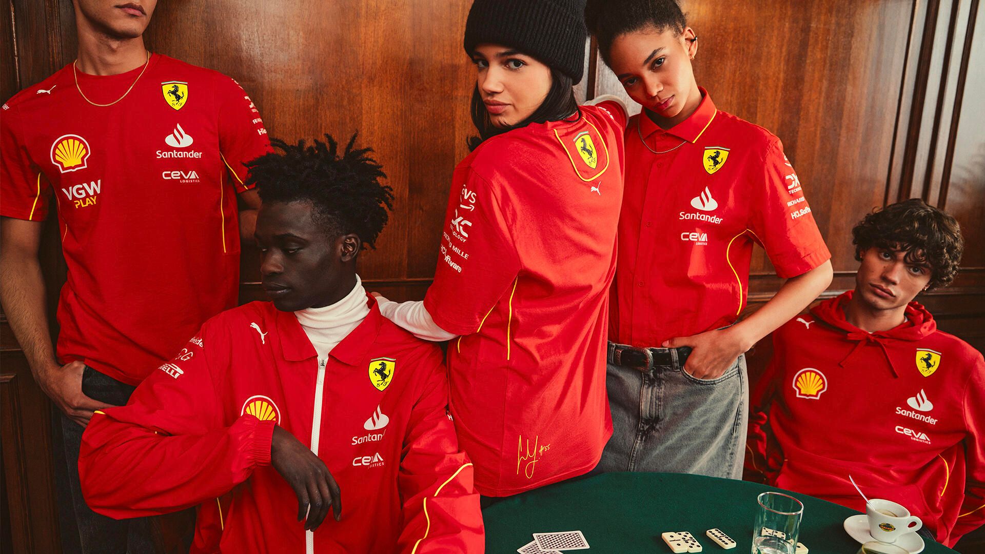 Five models pose in red Ferrari team apparel with sponsor logos around a green table.