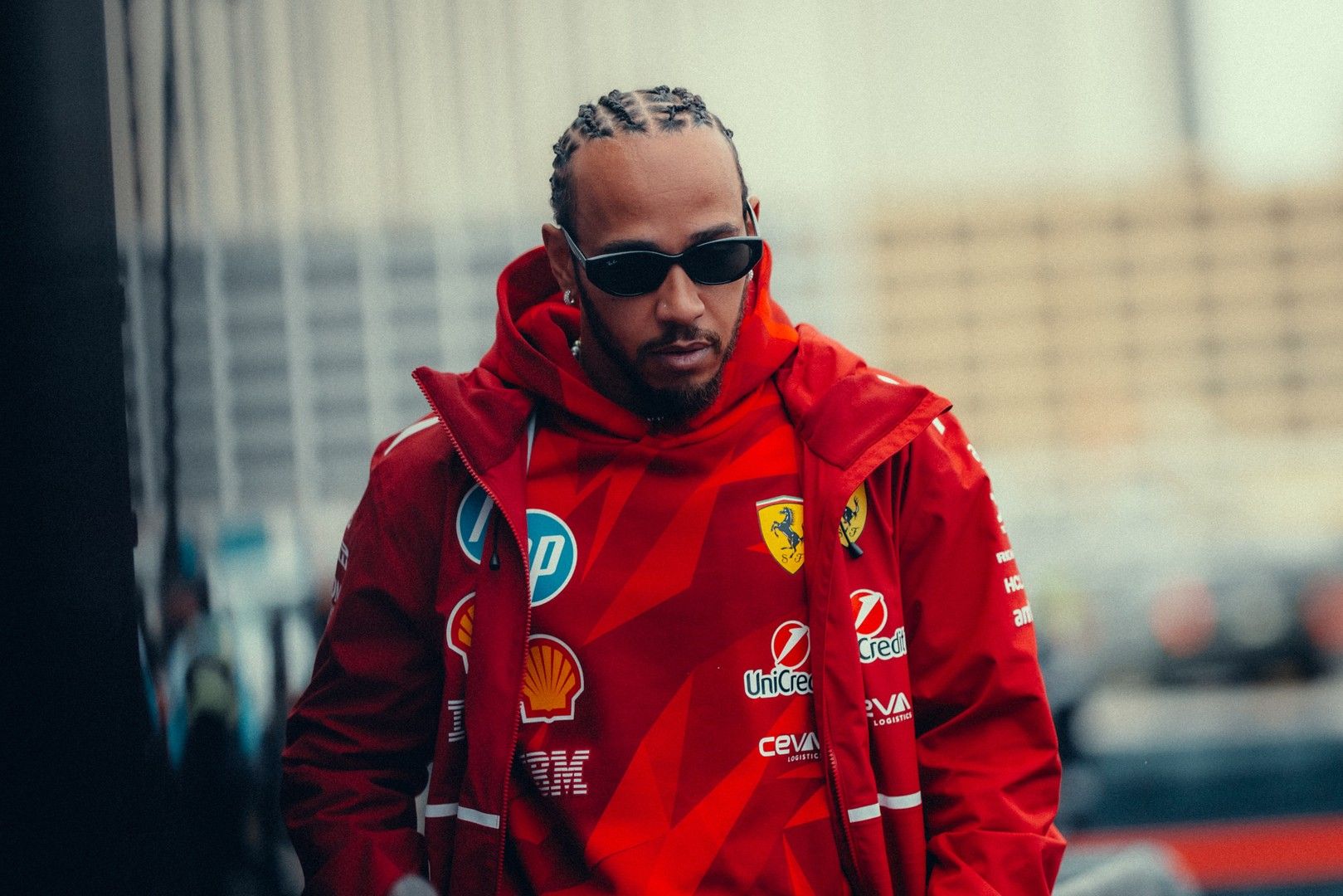Lewis Hamilton in a red jacket with a Ferrari logo and sunglasses.