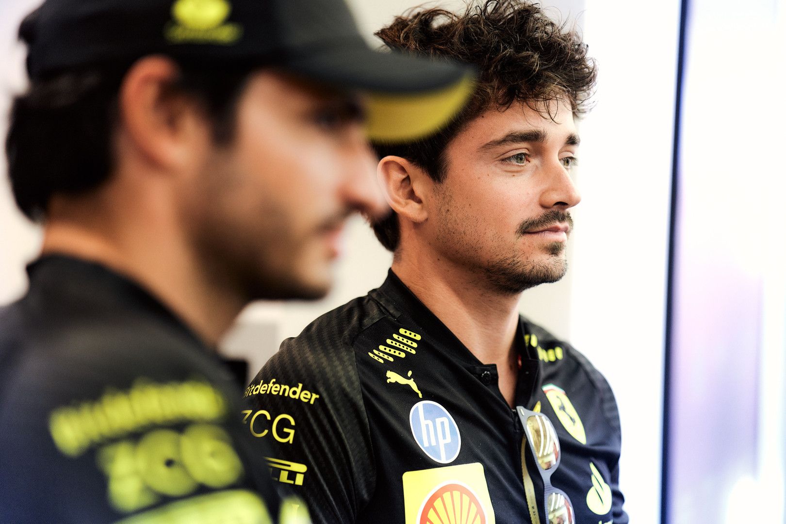 Formula 1 driver Charles Leclerc, in a black team shirt, looks intently to the right, with another person blurred in the foreground.