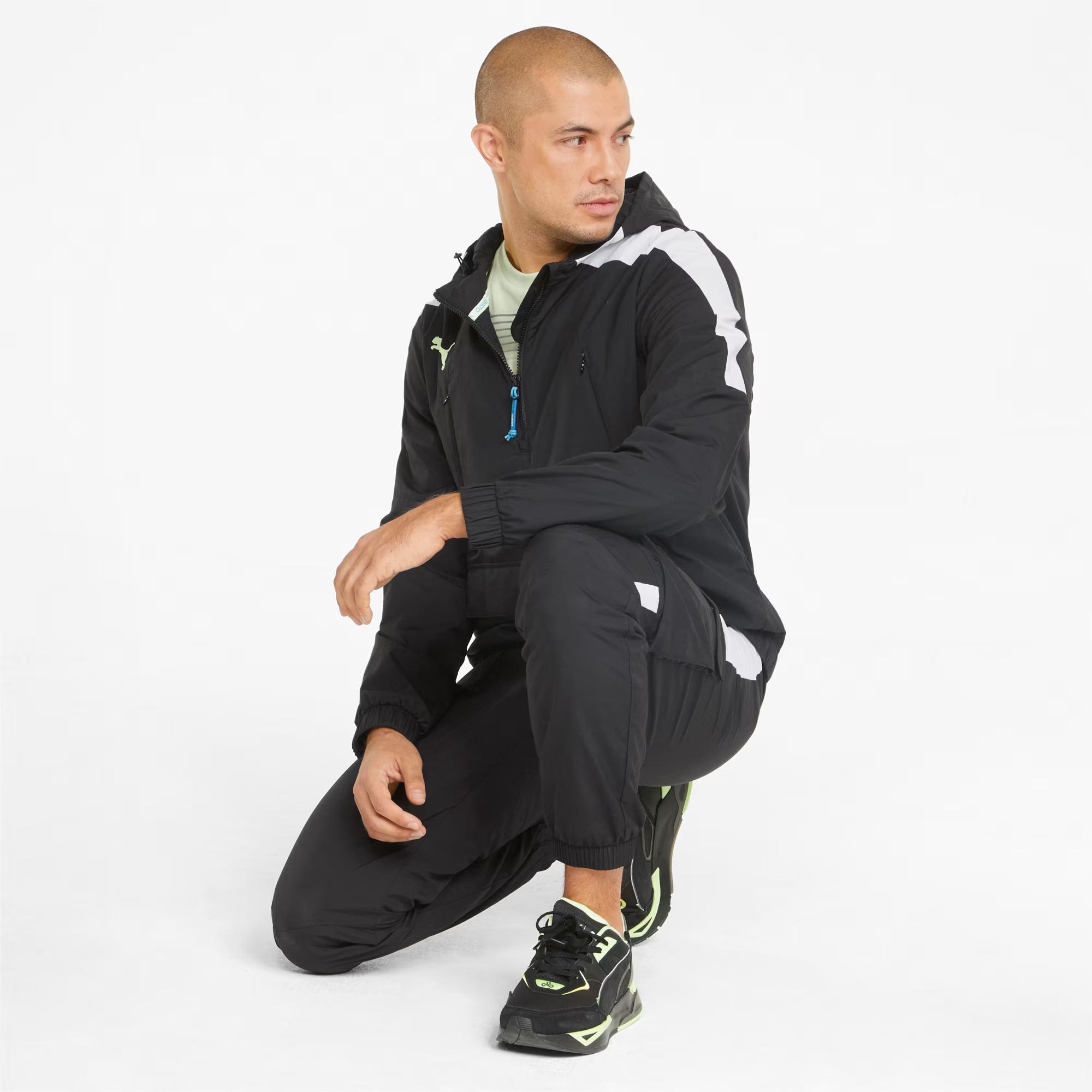A man in a black Puma track suit with white accents and black and neon yellow sneakers crouches, looking right.
