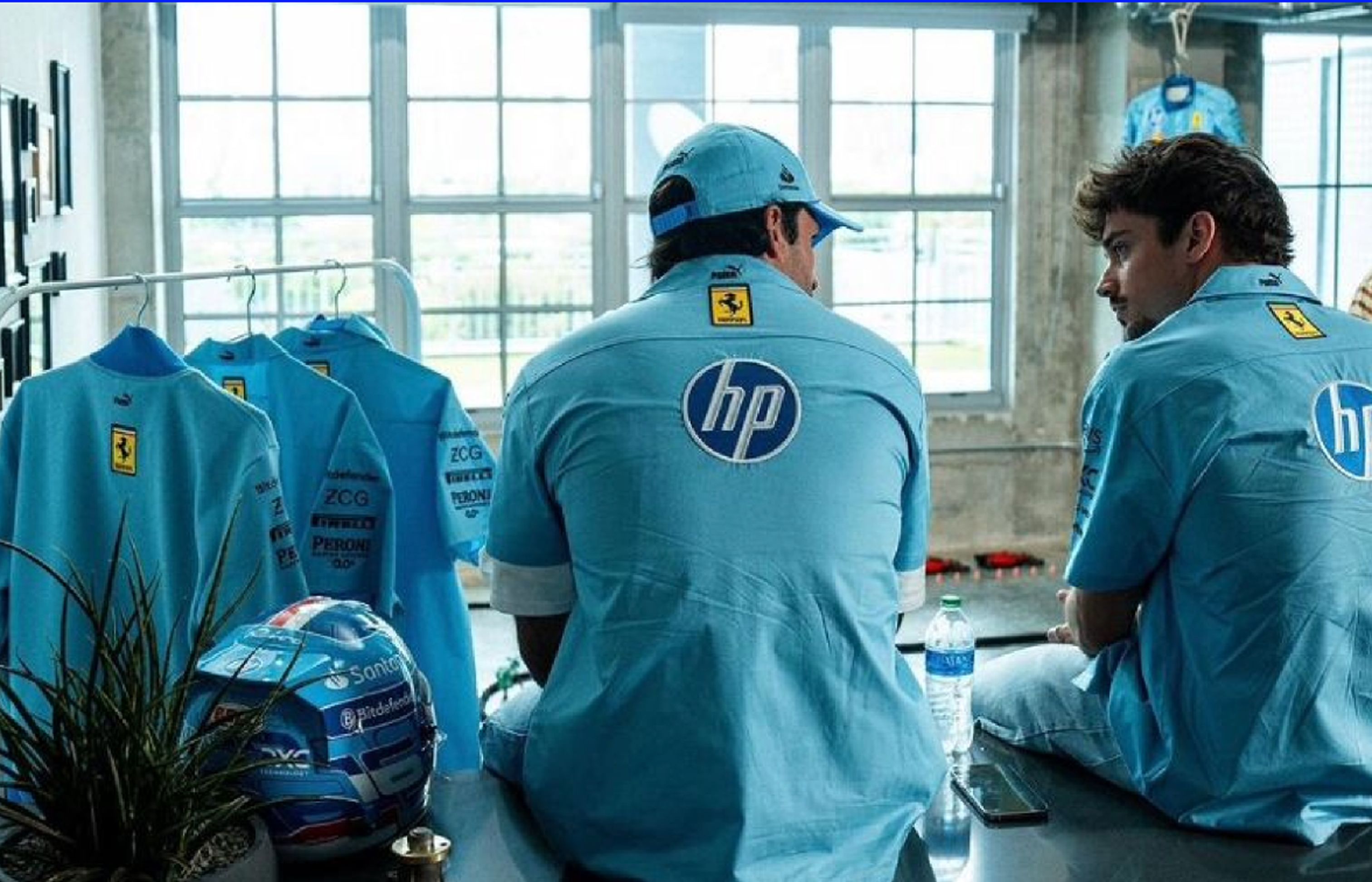 Two Ferrari F1 drivers, including Charles Leclerc, sit in light blue HP and Ferrari team shirts, with a matching helmet and gear visible.
