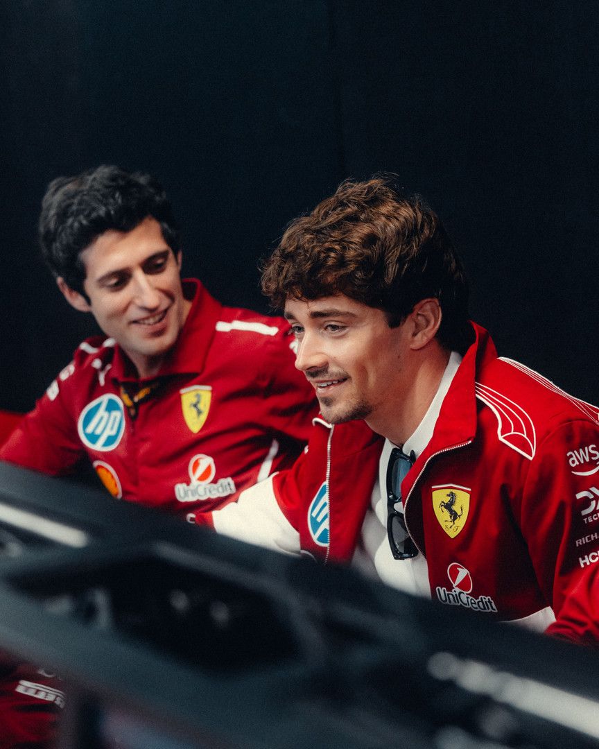 Carlos Sainz Jr. and Charles Leclerc smiling in red Ferrari team jackets.