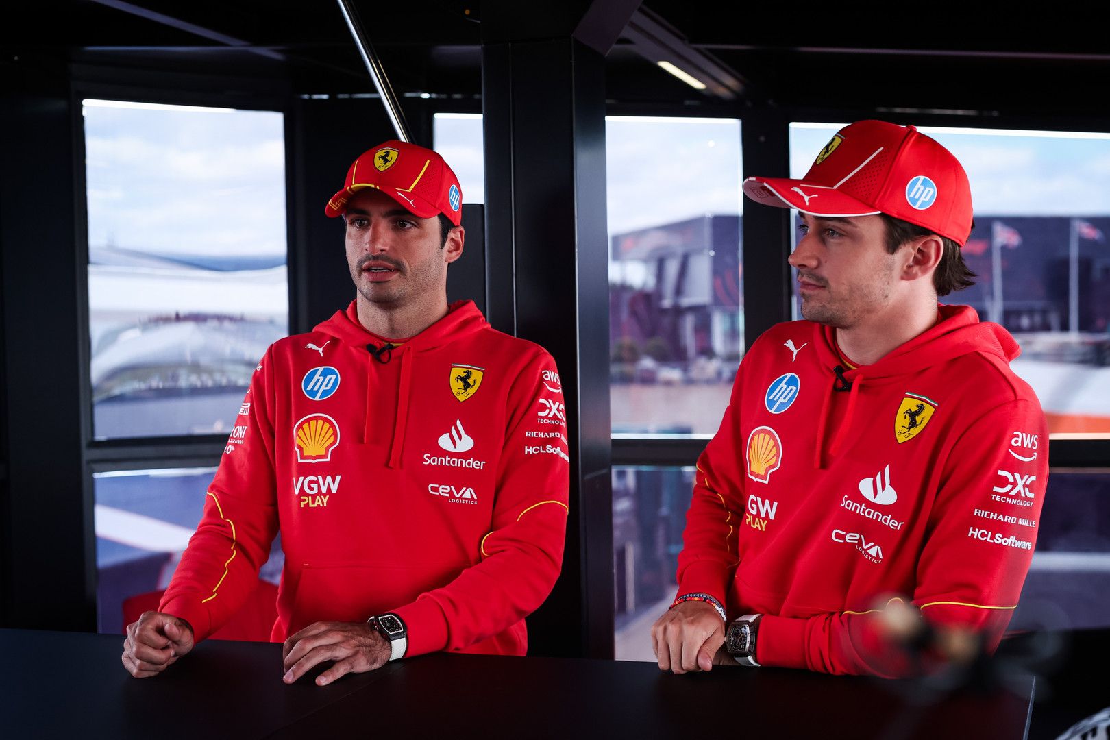 Carlos Sainz Jr. and Charles Leclerc in red Ferrari team hoodies and caps.