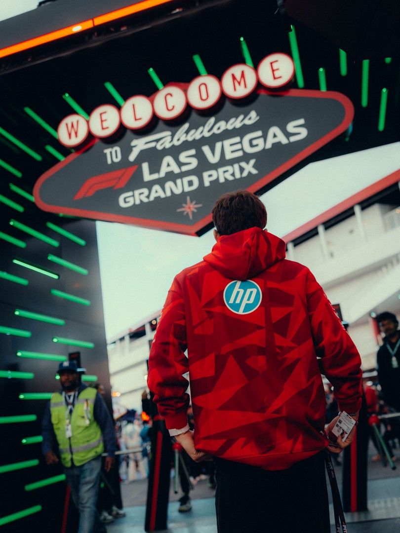 A person in a red HP hoodie stands facing a "Welcome to Fabulous Las Vegas Grand Prix" sign.