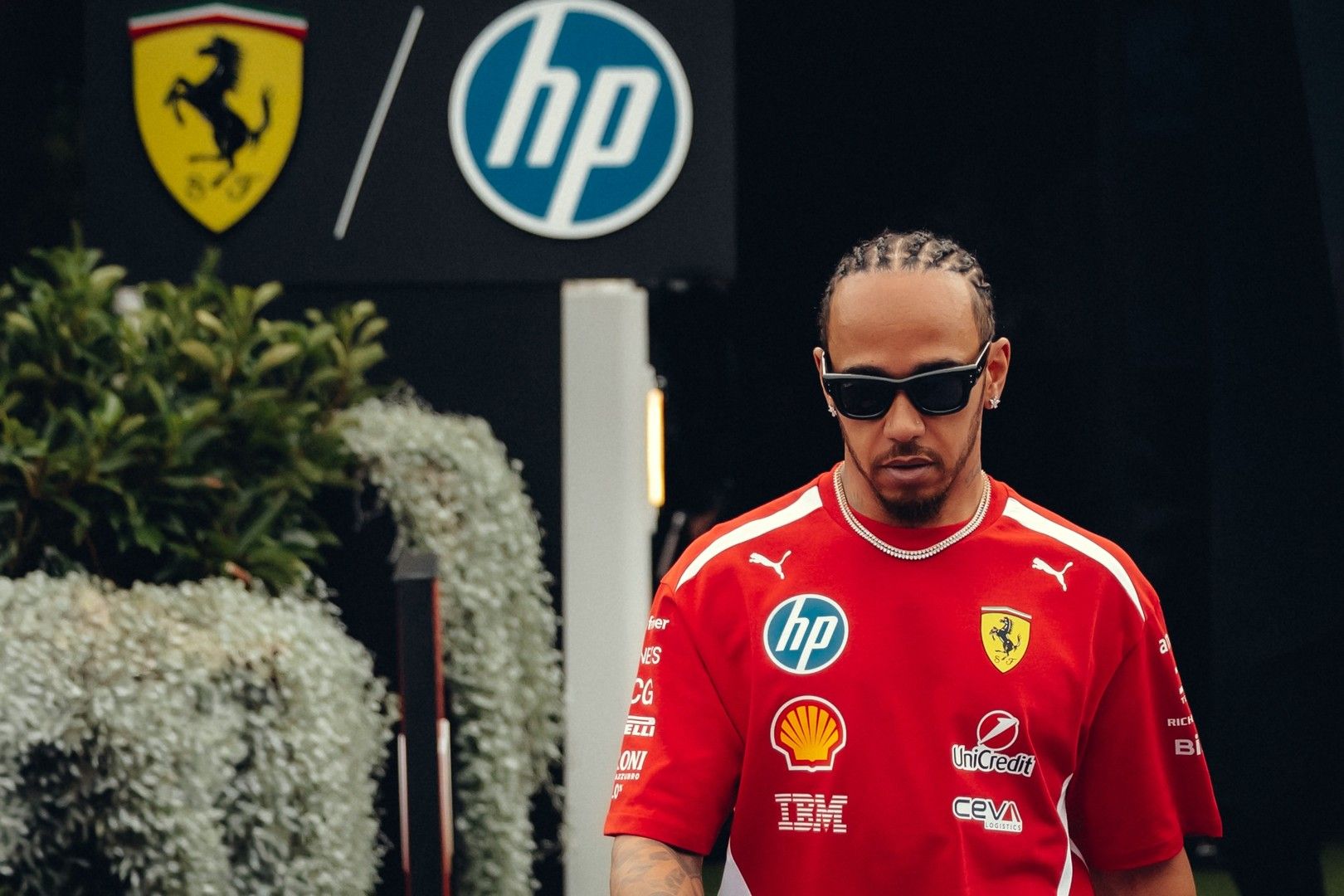 Lewis Hamilton in sunglasses and a red Ferrari team shirt, with Ferrari and HP logos in the background.