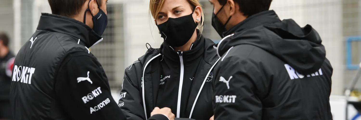 A woman and two men in black branded team jackets and face masks huddle outdoors.