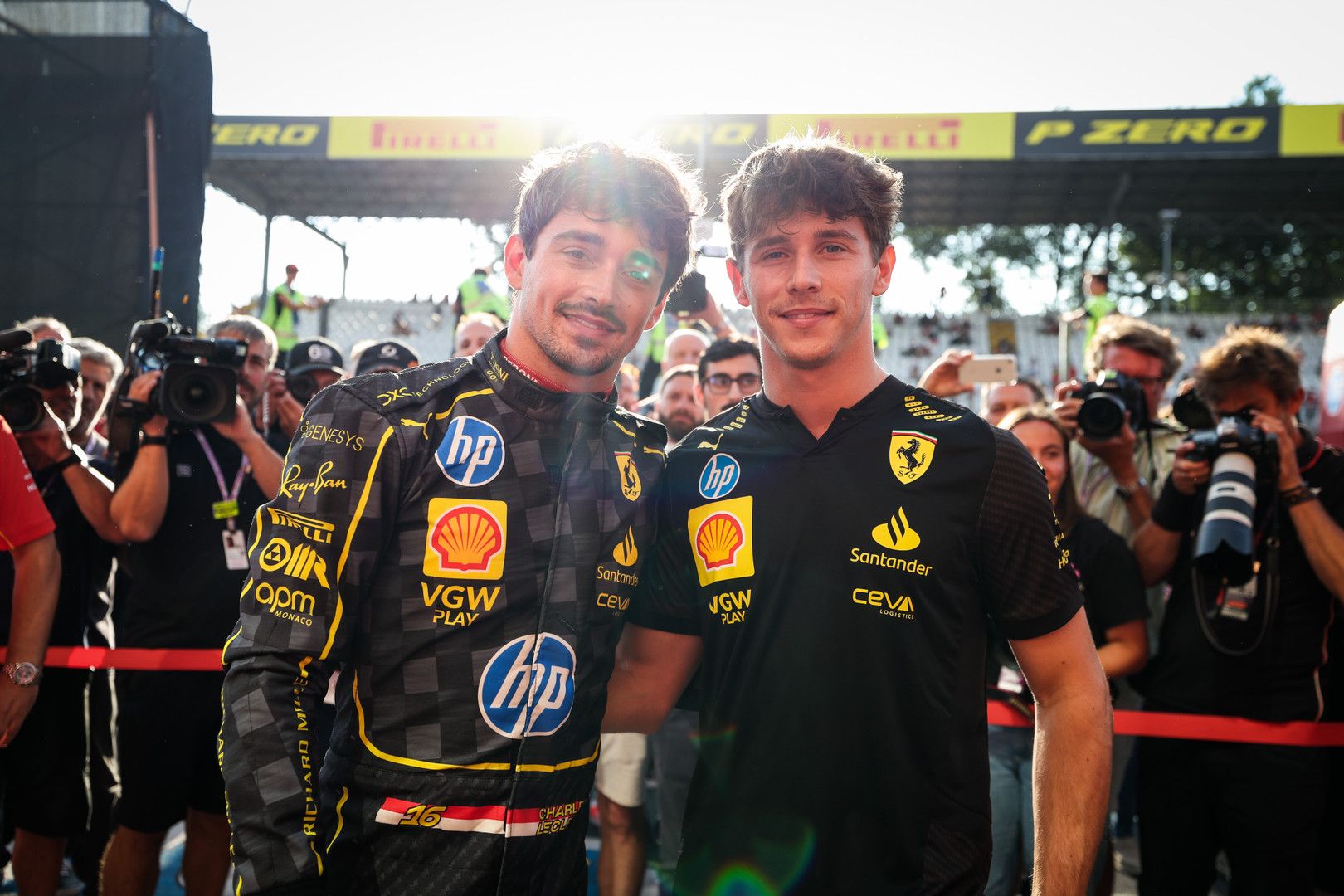 Brothers Charles Leclerc in a racing suit and Arthur Leclerc in a black team shirt smiling at a sunny outdoor event.