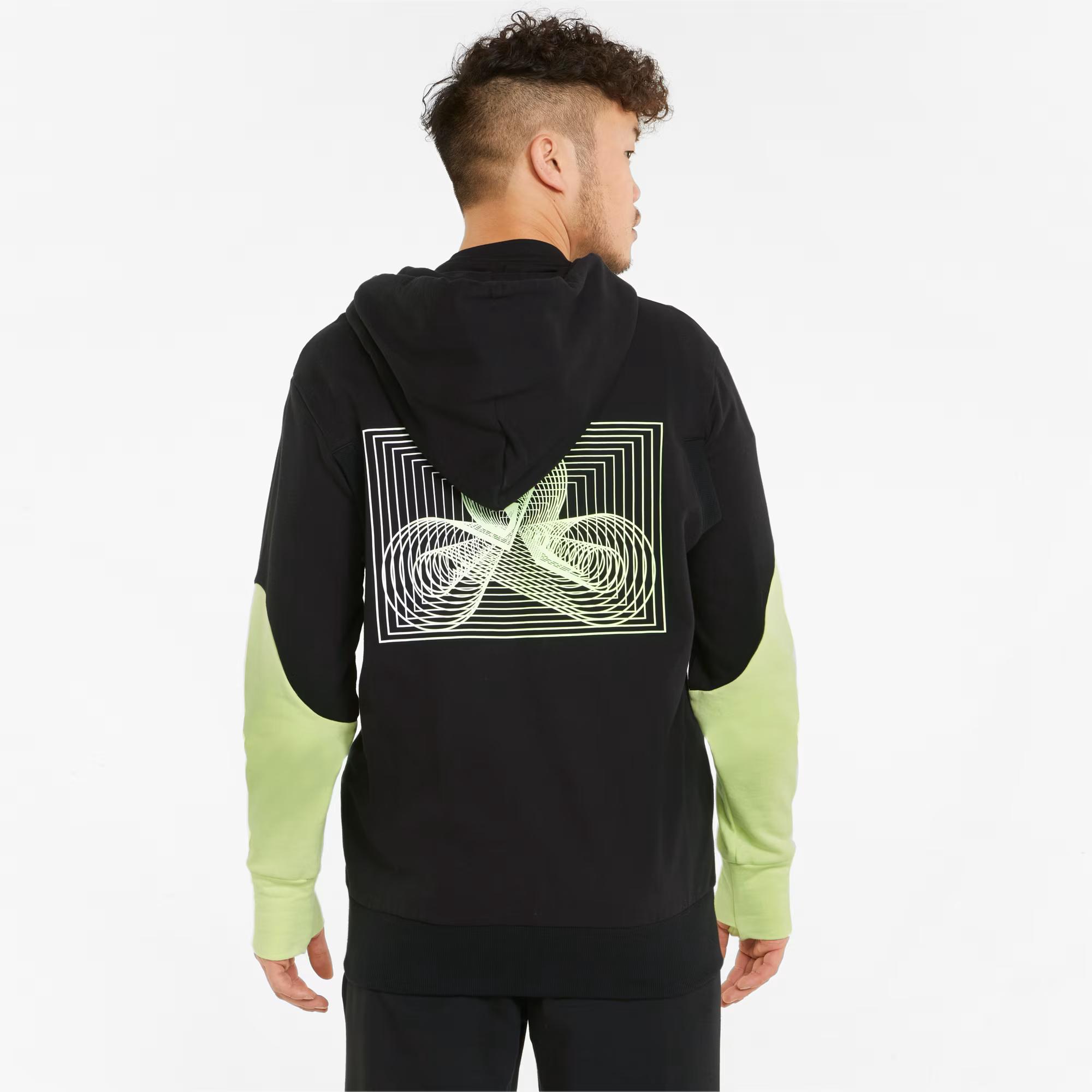 A person seen from the back wearing a black hoodie with lime green sleeves and a back graphic of a lime green swirling design within white concentric squares.