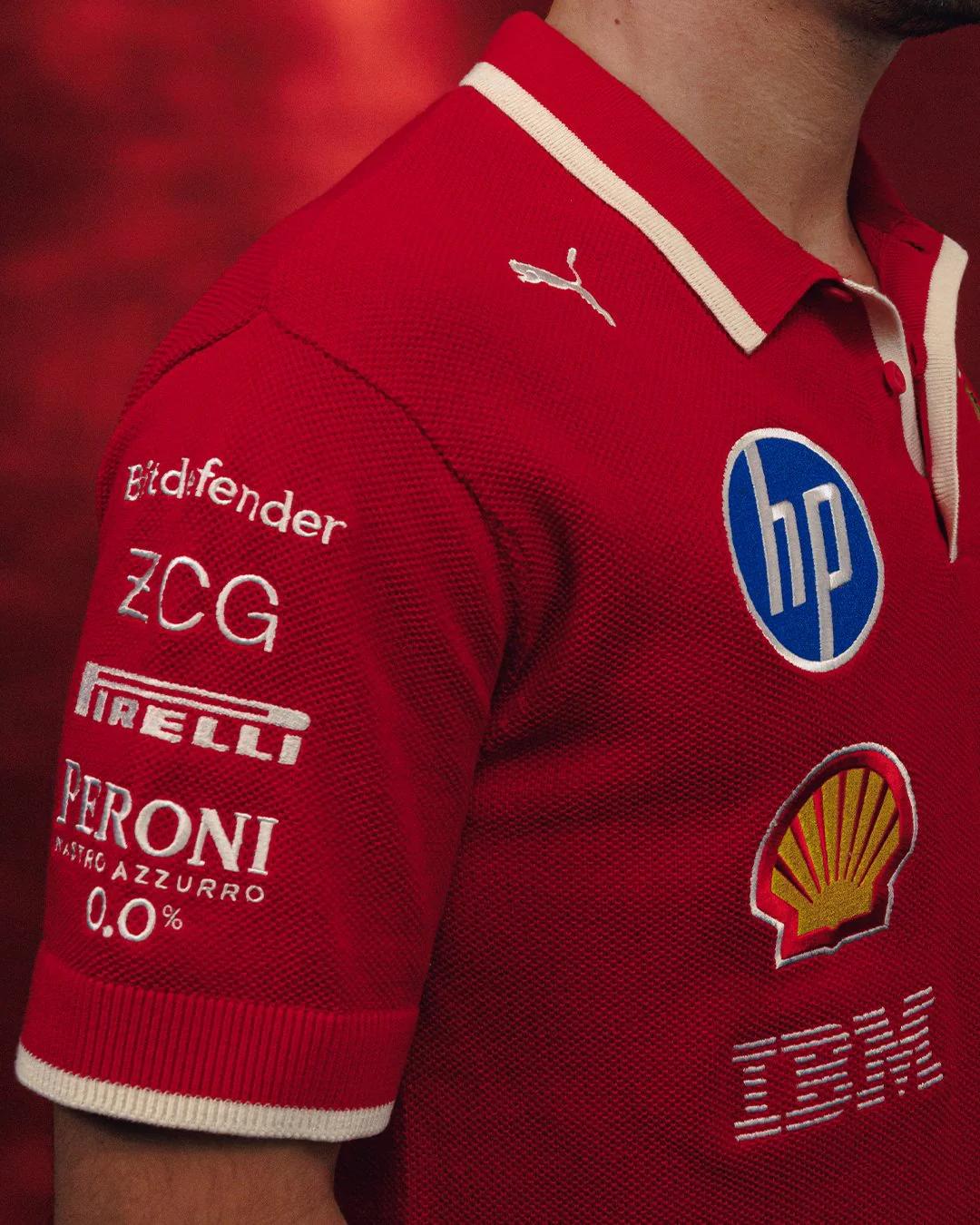 Close-up of a person wearing a red polo shirt with cream trim, featuring sponsor logos including Puma, Bitdefender, ZCG, Pirelli, Peroni, HP, Shell, and IBM.