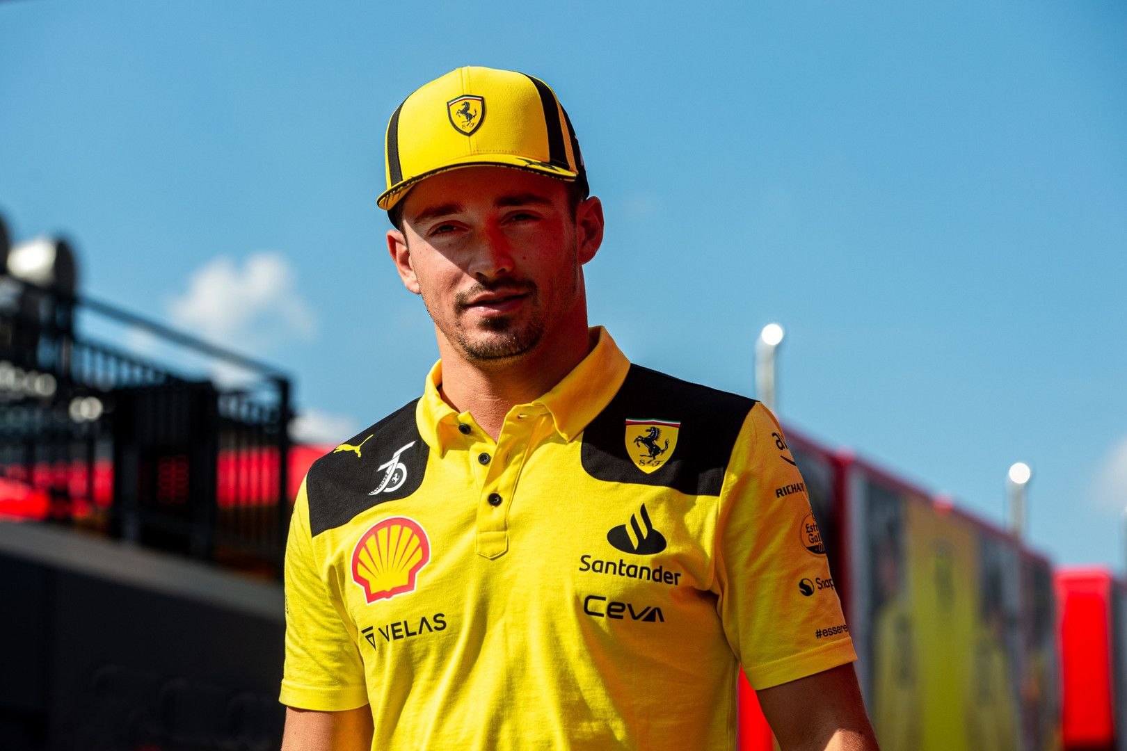 Charles Leclerc wearing a yellow Ferrari polo shirt and cap, looking at the camera.