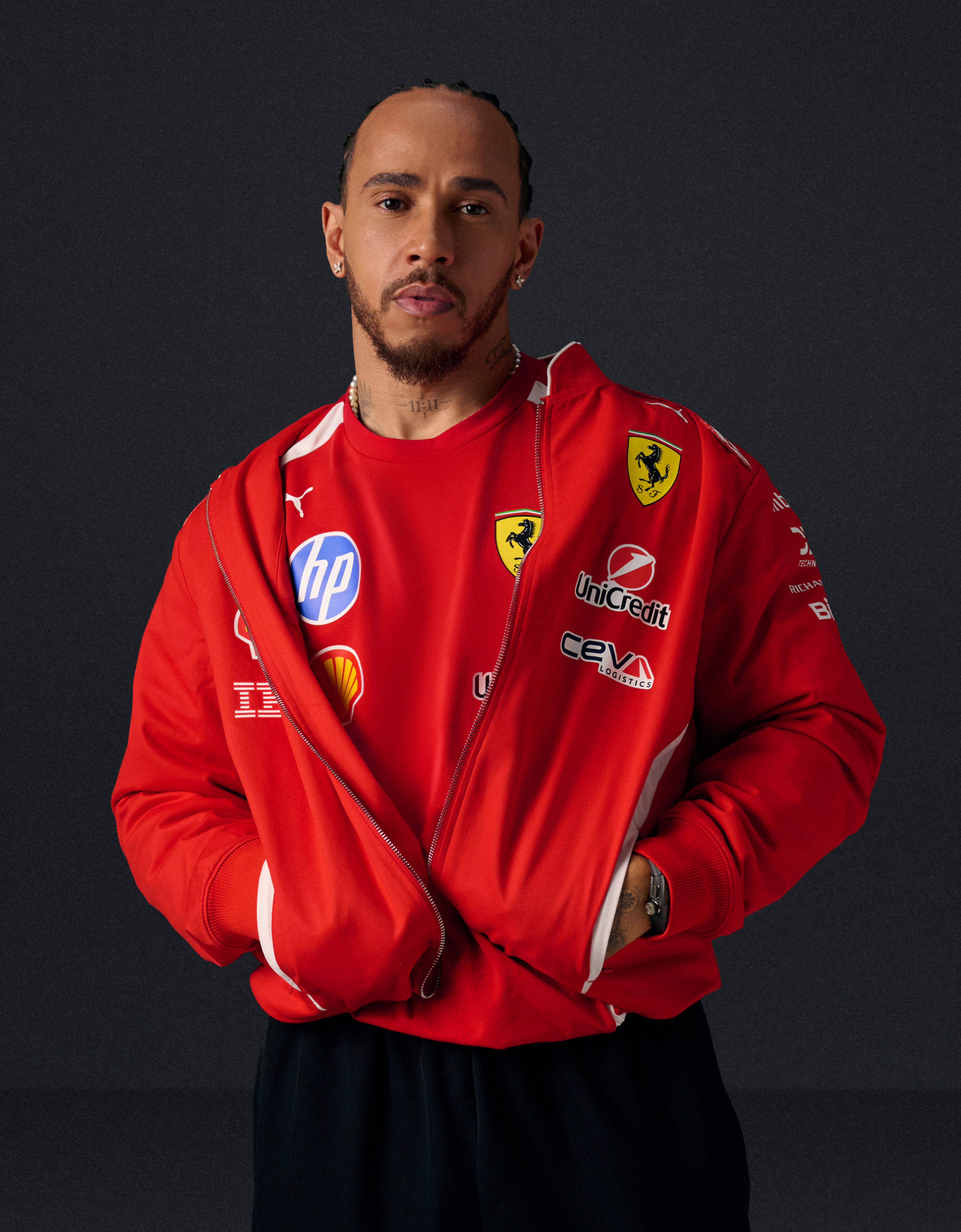 Lewis Hamilton in a red Ferrari team jacket, looking at the viewer.