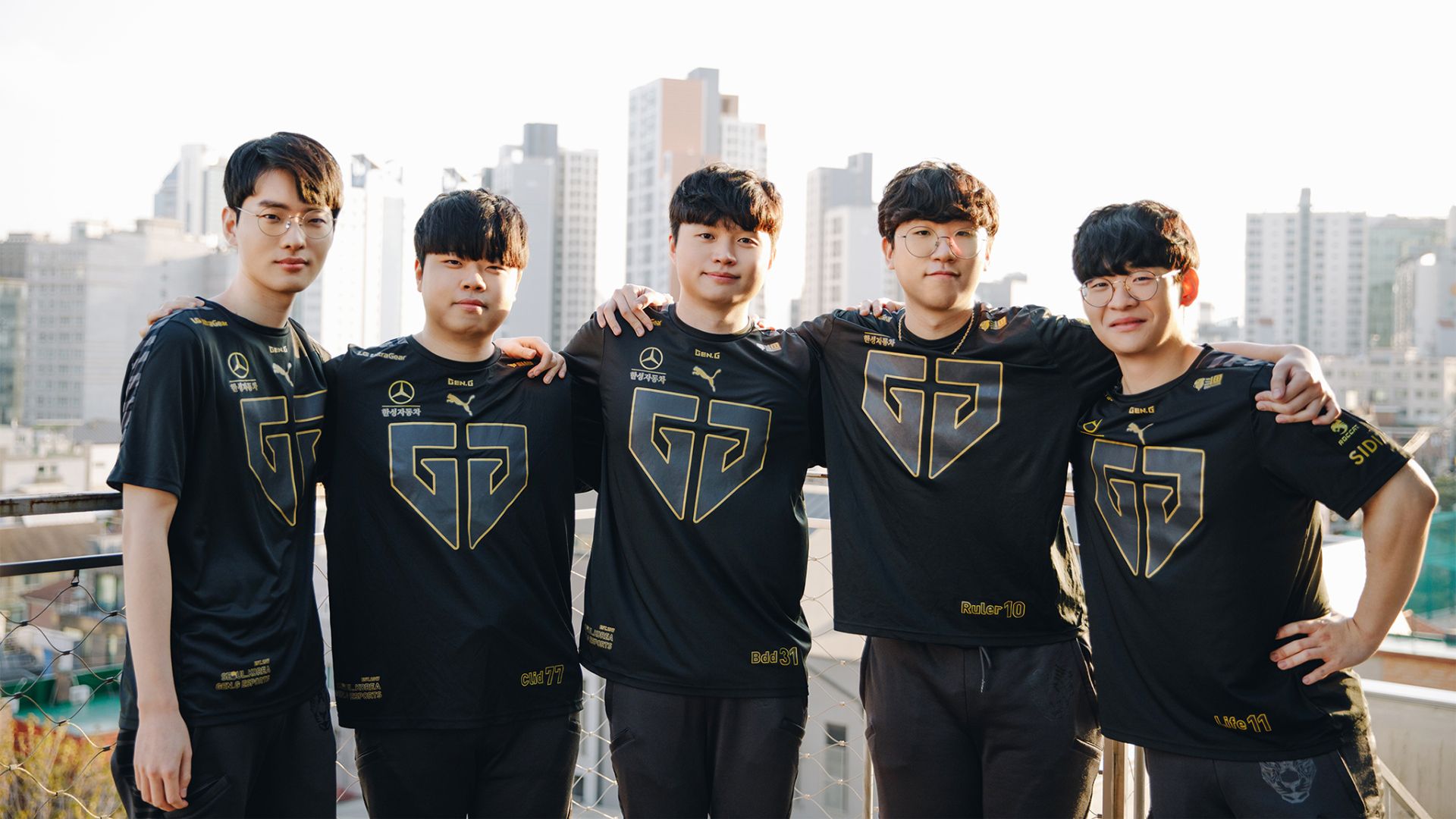 Five esports players in black and gold GG jerseys pose outdoors with a cityscape.