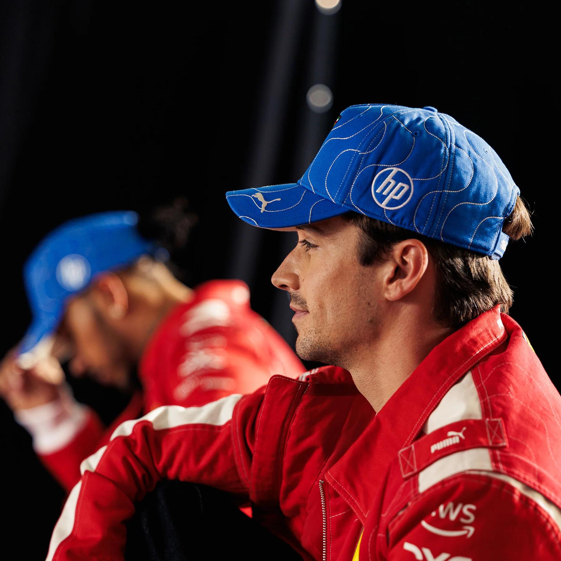 A man in a red racing suit wearing a blue cap with HP and Puma logos.
