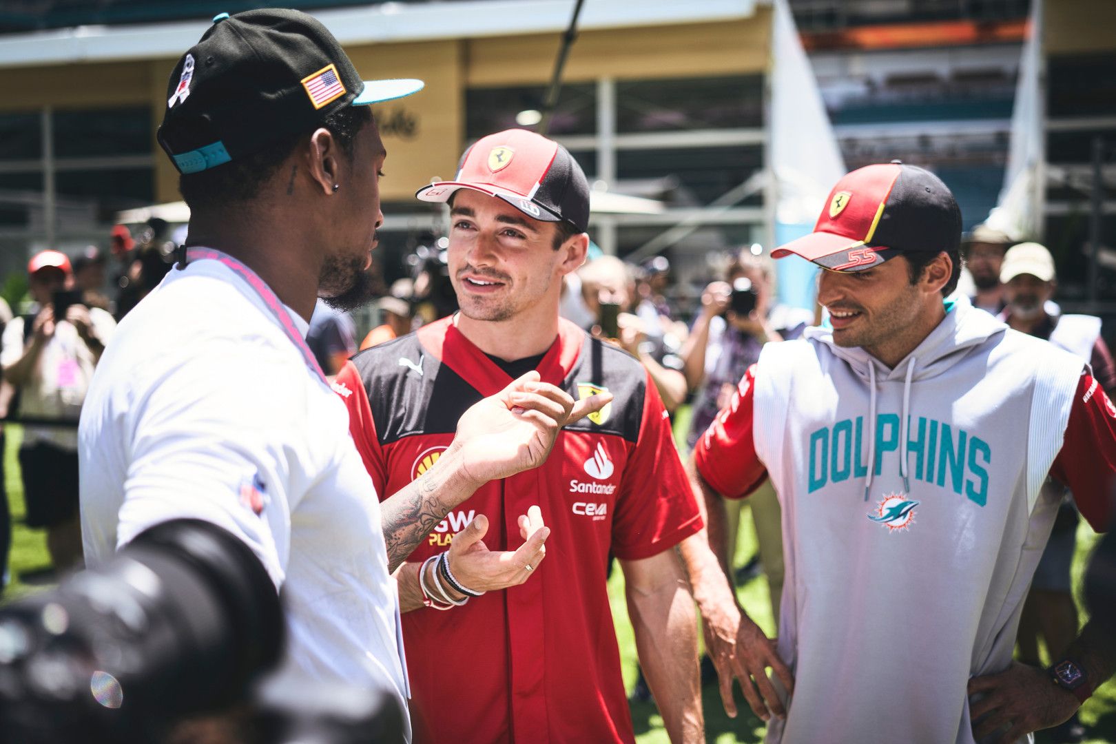 Formula 1 drivers Charles Leclerc and Carlos Sainz, with Sainz wearing a Dolphins hoodie, talk with a man in a black cap.