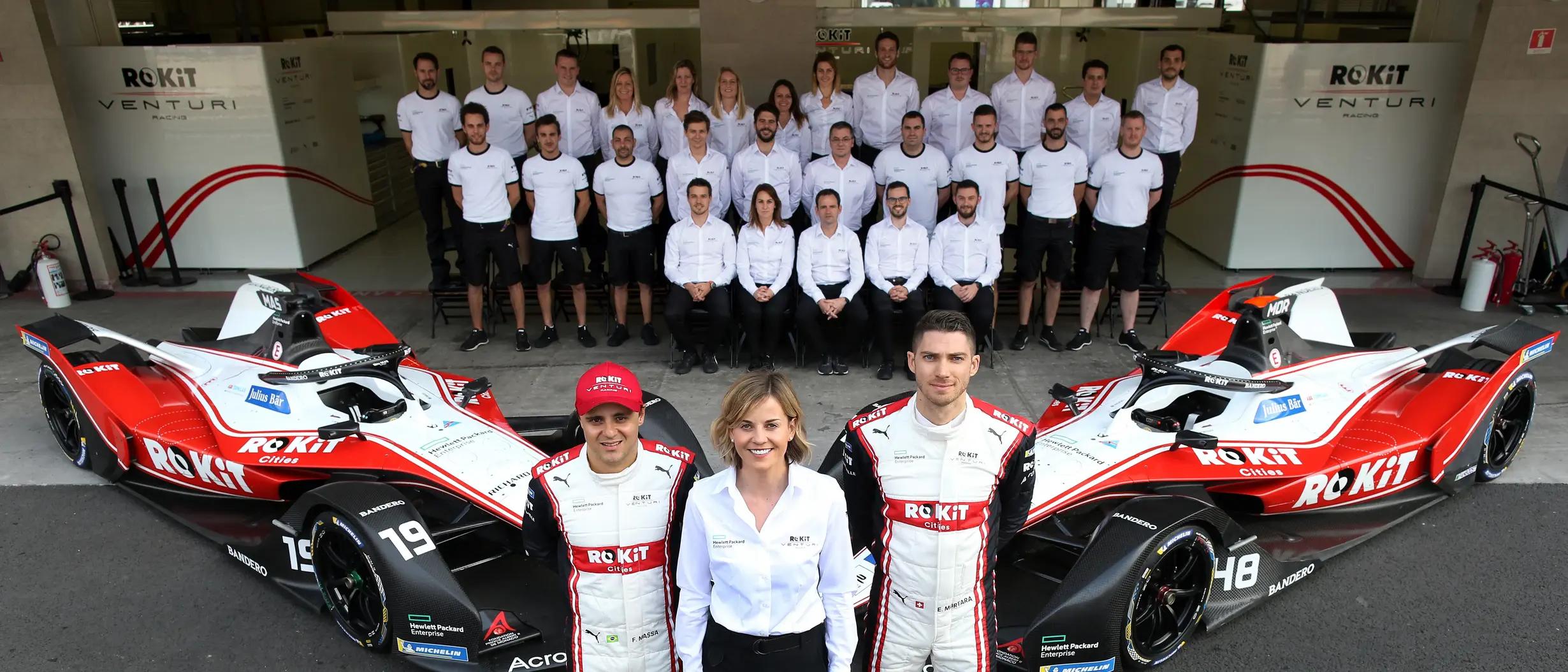 ROKiT Venturi Formula E team, including two drivers and a woman, posing with two red and white race cars and other team members.