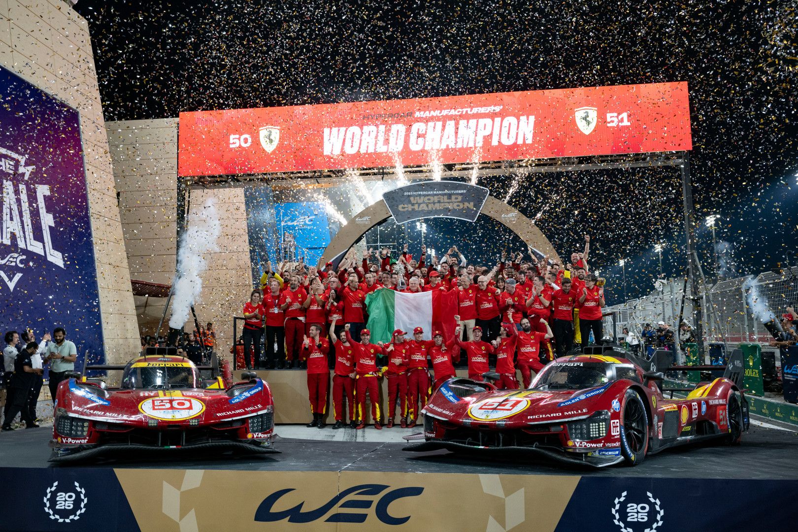 Ferrari team celebrates winning the World Champion title with two red racing cars, an Italian flag, and falling confetti.