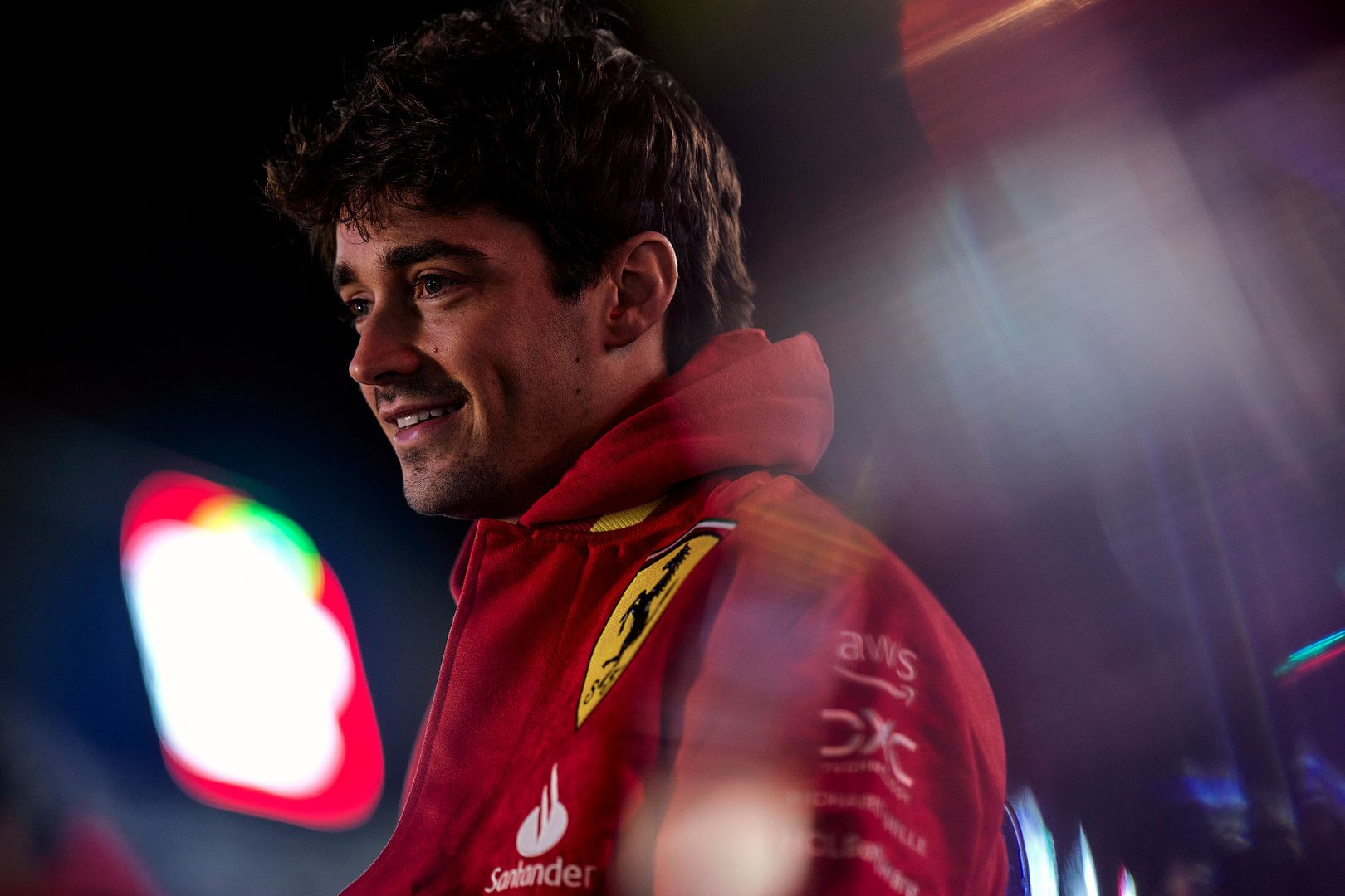 Charles Leclerc smiles in a red Ferrari team jacket.