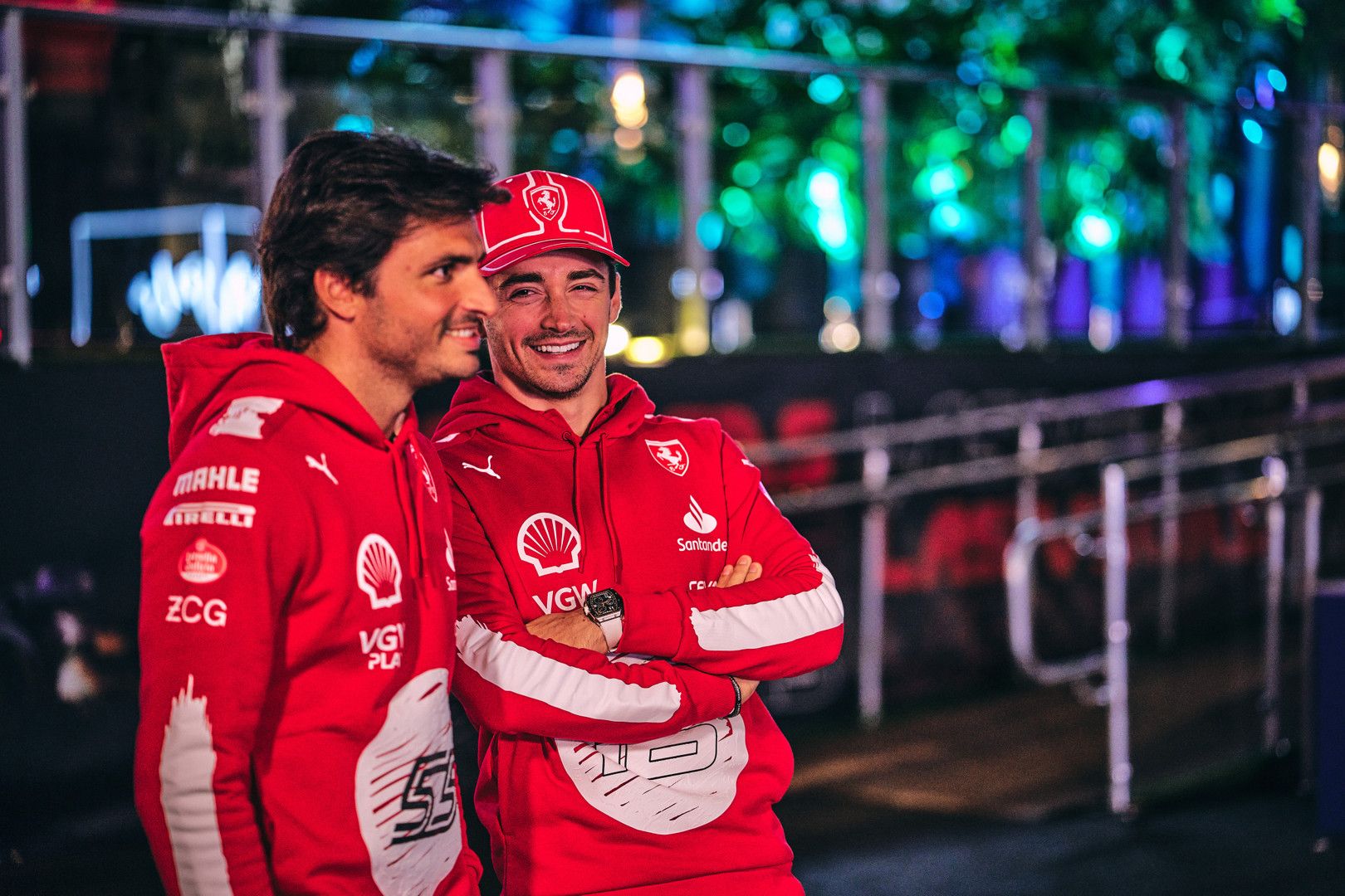 Formula 1 drivers Charles Leclerc and Carlos Sainz Jr. smile in red Ferrari team hoodies.