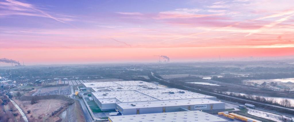 Aerial view of a large amazon.de fulfillment warehouse at pink sunrise with surrounding fields