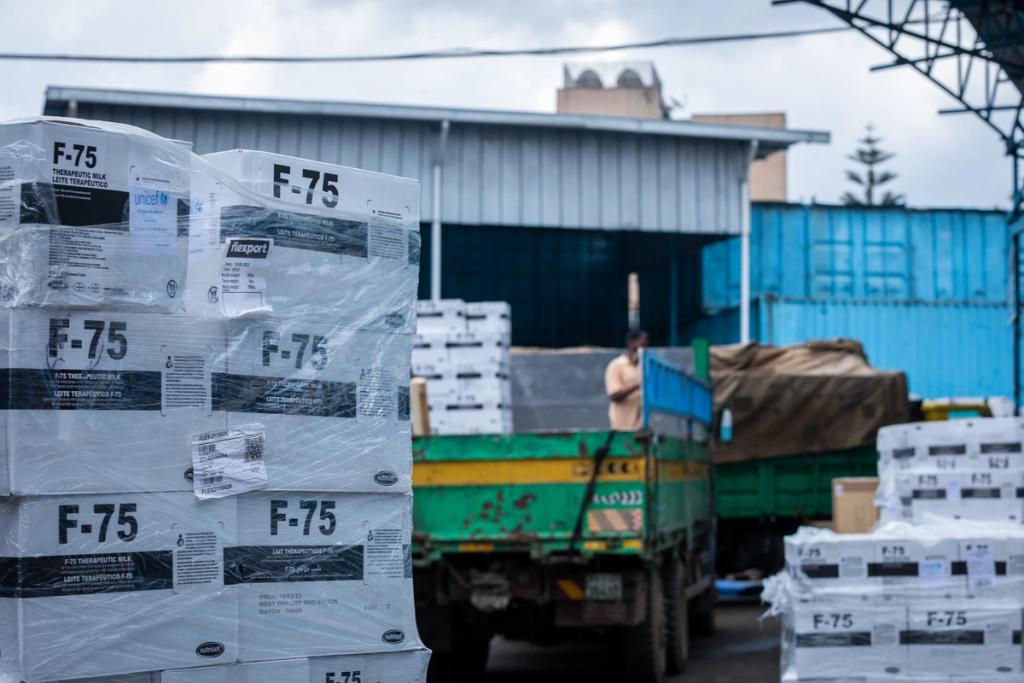 Pallets of UNICEF F-75 therapeutic milk in Flexport-labeled wrap beside trucks at a warehouse yard.