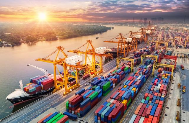 Aerial view of a container port at sunset with gantry cranes, a docked container ship and rows of colorful containers along a river
