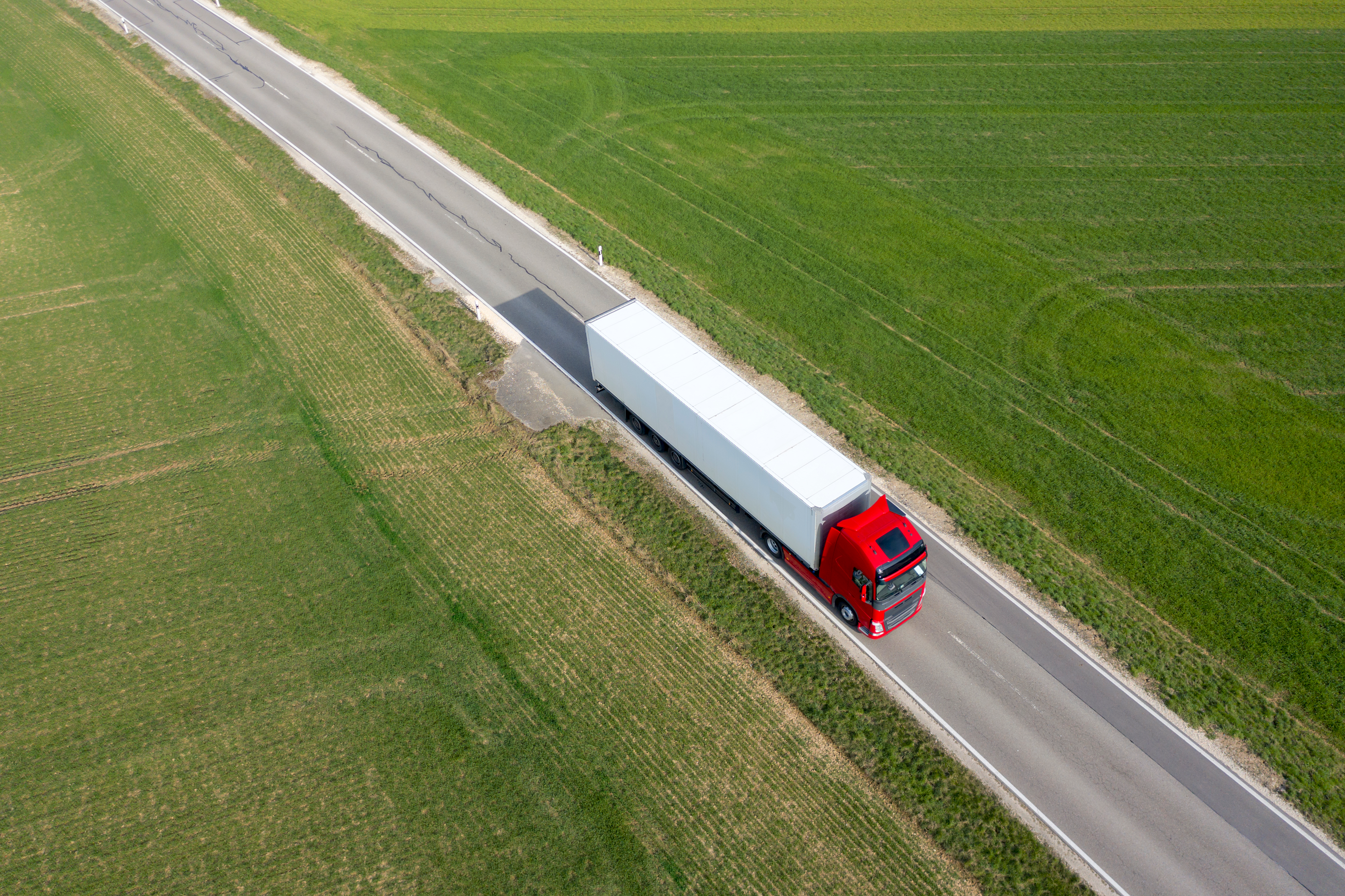 Aerial view of a semi-truck traveling on a highway between agricultural fields.