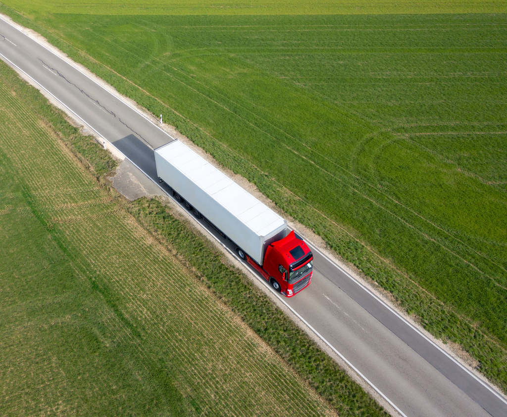 Aerial view of a semi-truck traveling on a highway between agricultural fields.