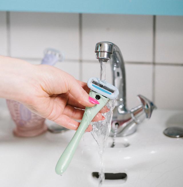 Hand rinsing a mint-green Estrid razor under a running bathroom faucet