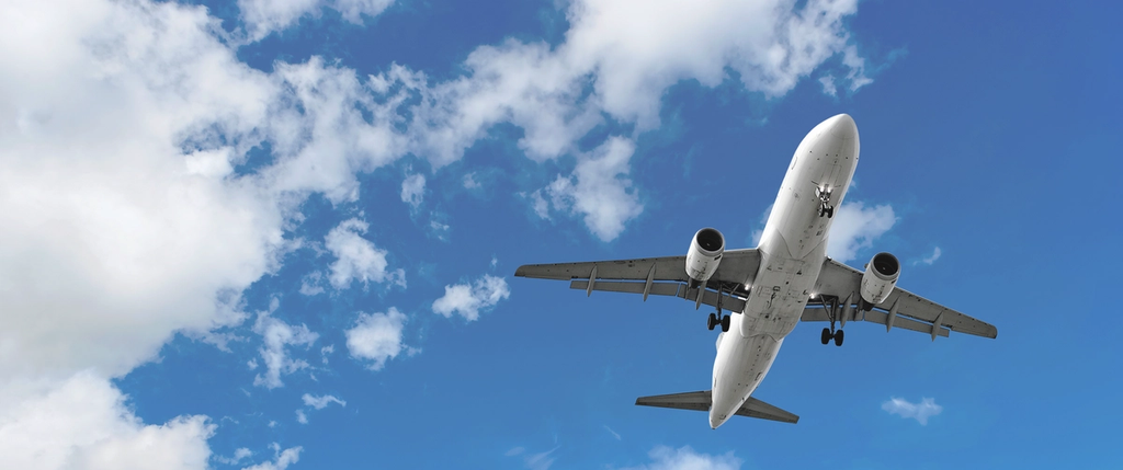 A commercial aircraft in flight approaches for landing against a cloudy sky.
