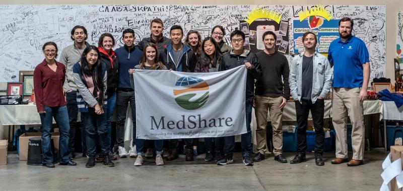Group of volunteers holding a MedShare banner in a warehouse with a graffiti-covered wall behind