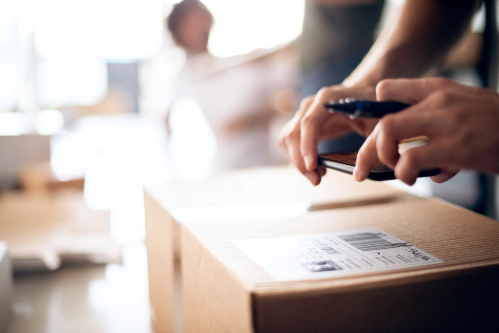 Close-up of hands scanning a barcode label on a cardboard parcel with a smartphone