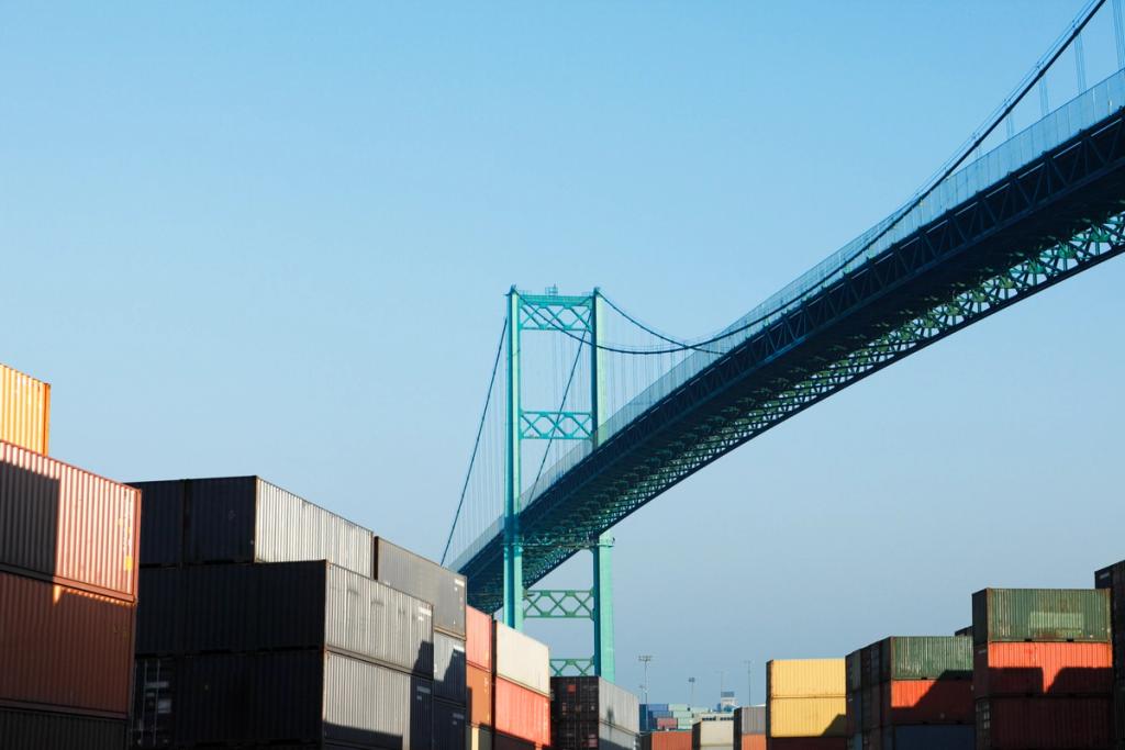 Stacked shipping containers at port beneath the green Vincent Thomas suspension bridge under a clear sky