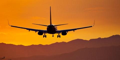 Silhouette of an airplane on approach at sunset over mountains in an orange sky