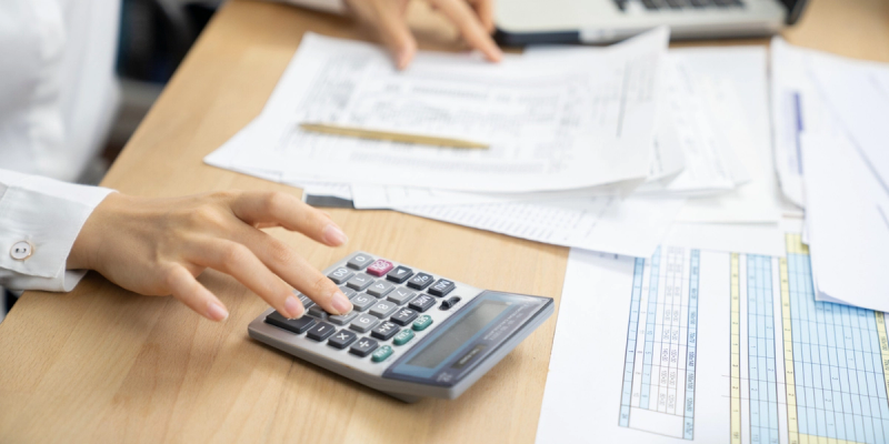 Person using a calculator over invoices and spreadsheets on a desk