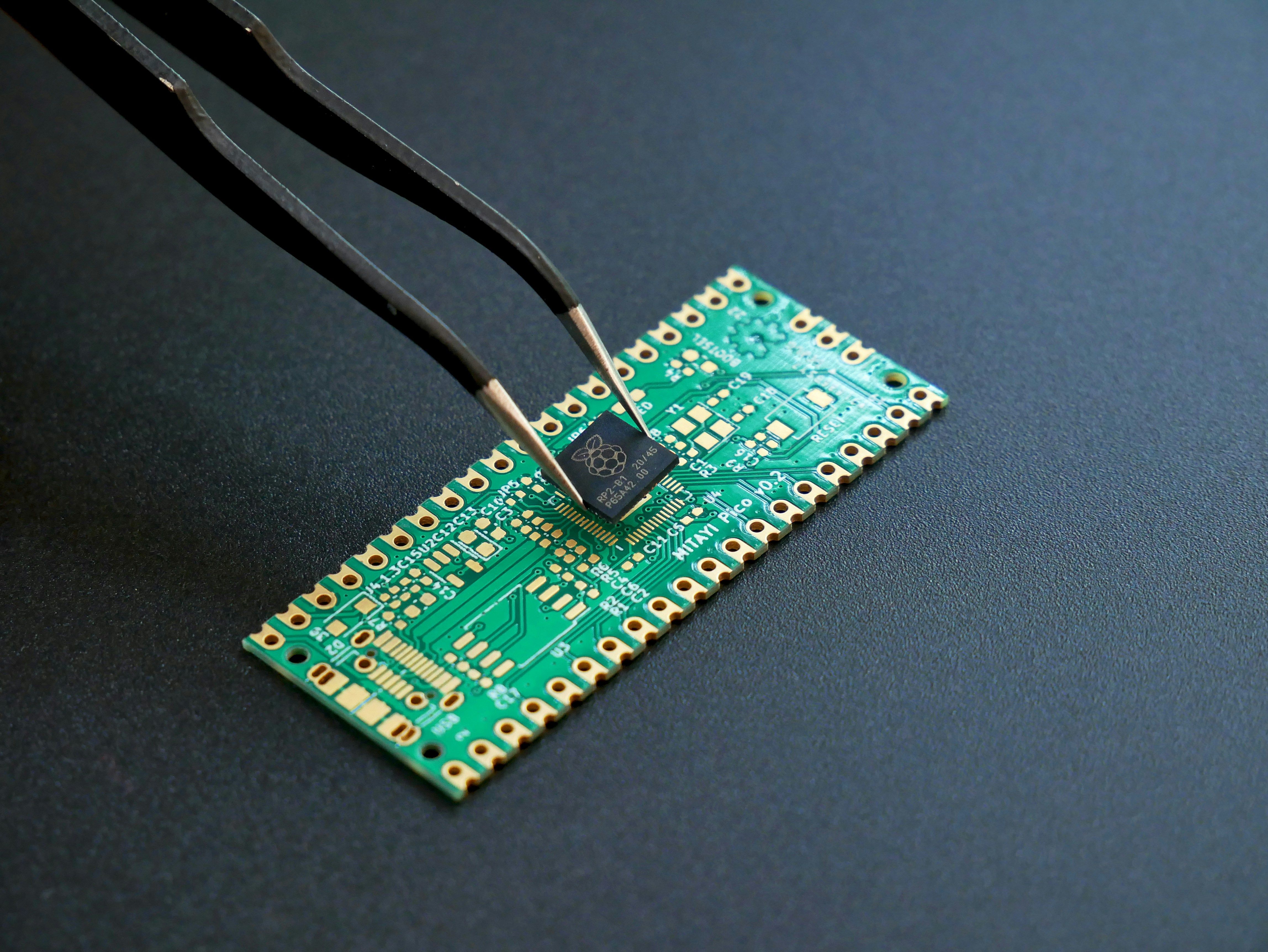 Tweezers placing a small semiconductor chip onto the pads of a green circuit board