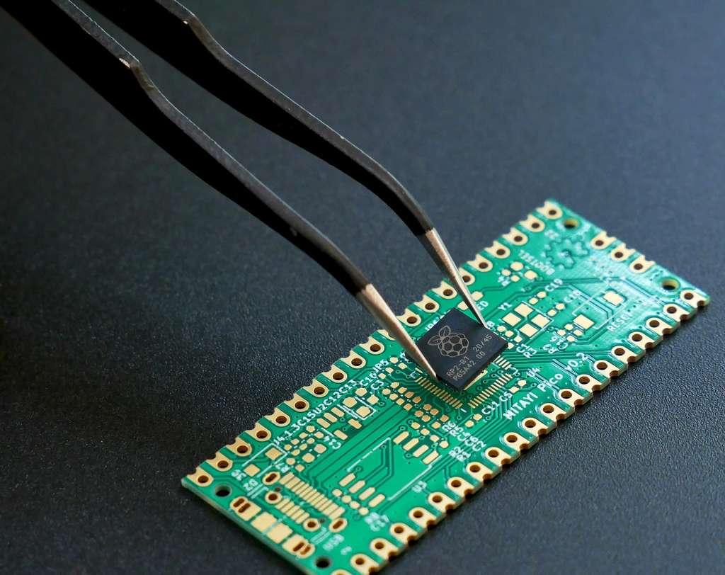 Tweezers placing a small semiconductor chip onto the pads of a green circuit board