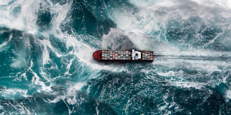 Aerial view of a container ship cutting through rough, churning ocean waves