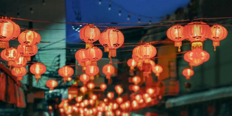 Red Chinese paper lanterns strung across a street glowing at dusk