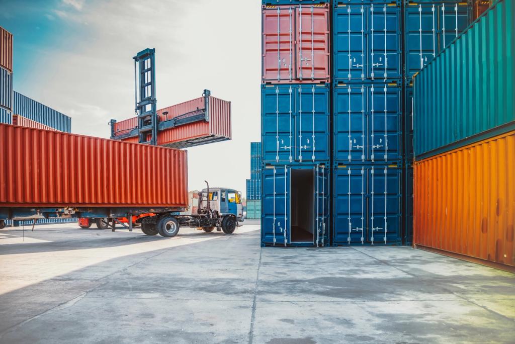 Container handling equipment loads shipping containers onto a truck at a port facility.