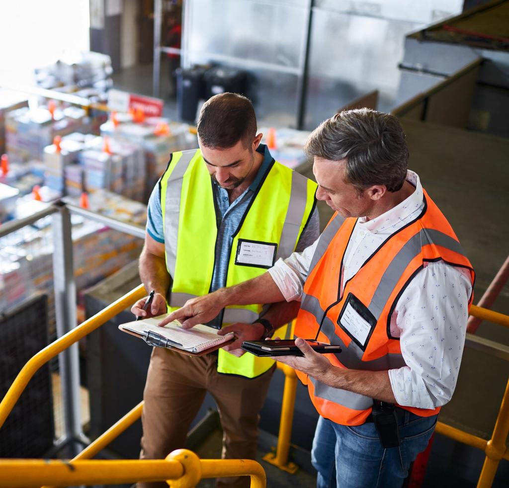 Two construction workers review paperwork at a construction site overlooking the work area.