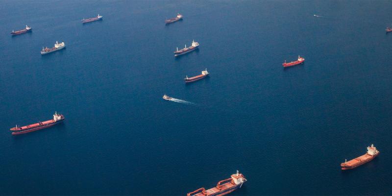 Aerial view of numerous bulk cargo ships anchored across dark blue open water