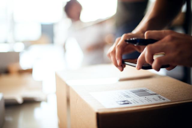 Close-up of hands scanning a barcode label on a cardboard parcel with a smartphone