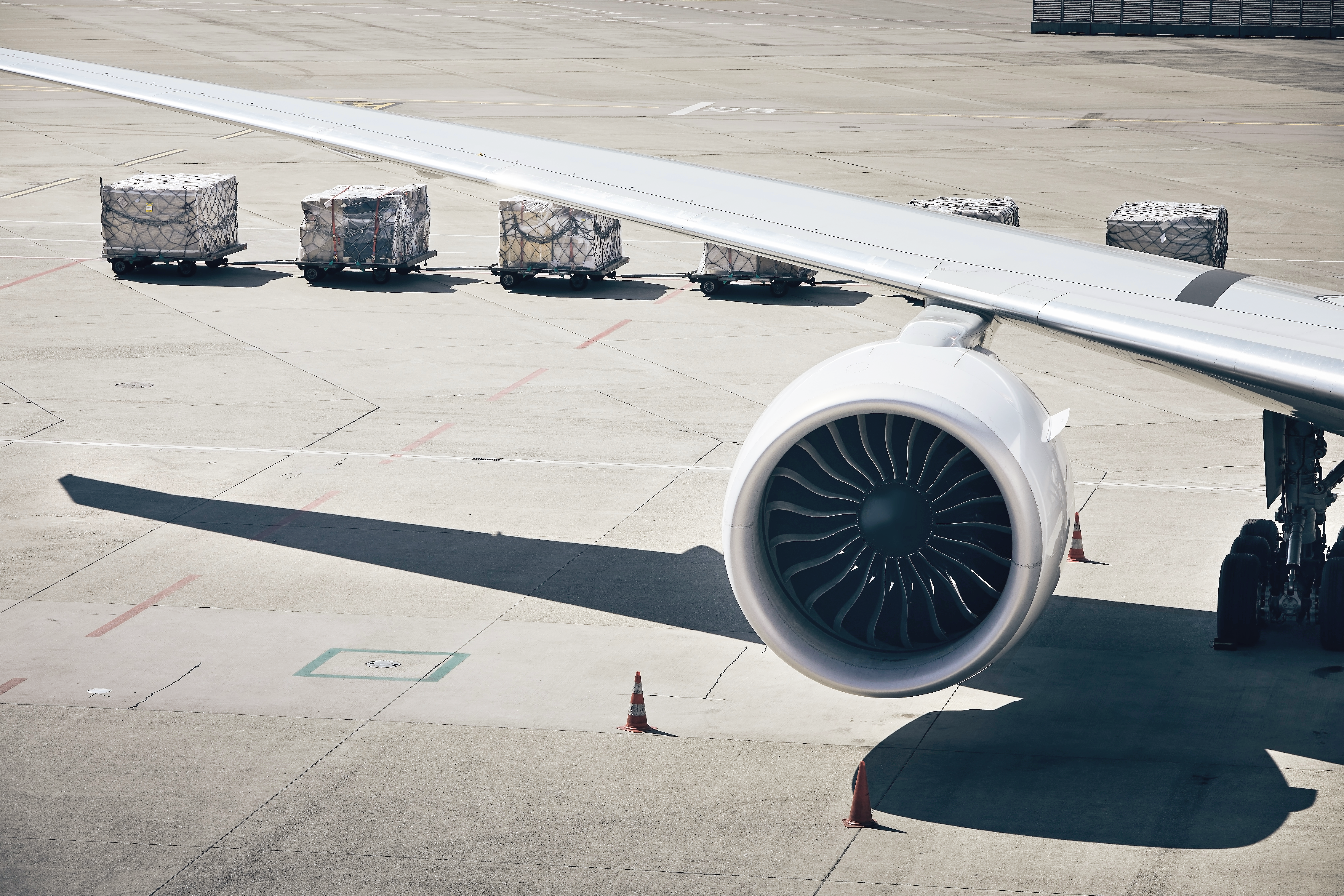 An aircraft engine and wing mounted on the tarmac beside cargo containers ready for loading.