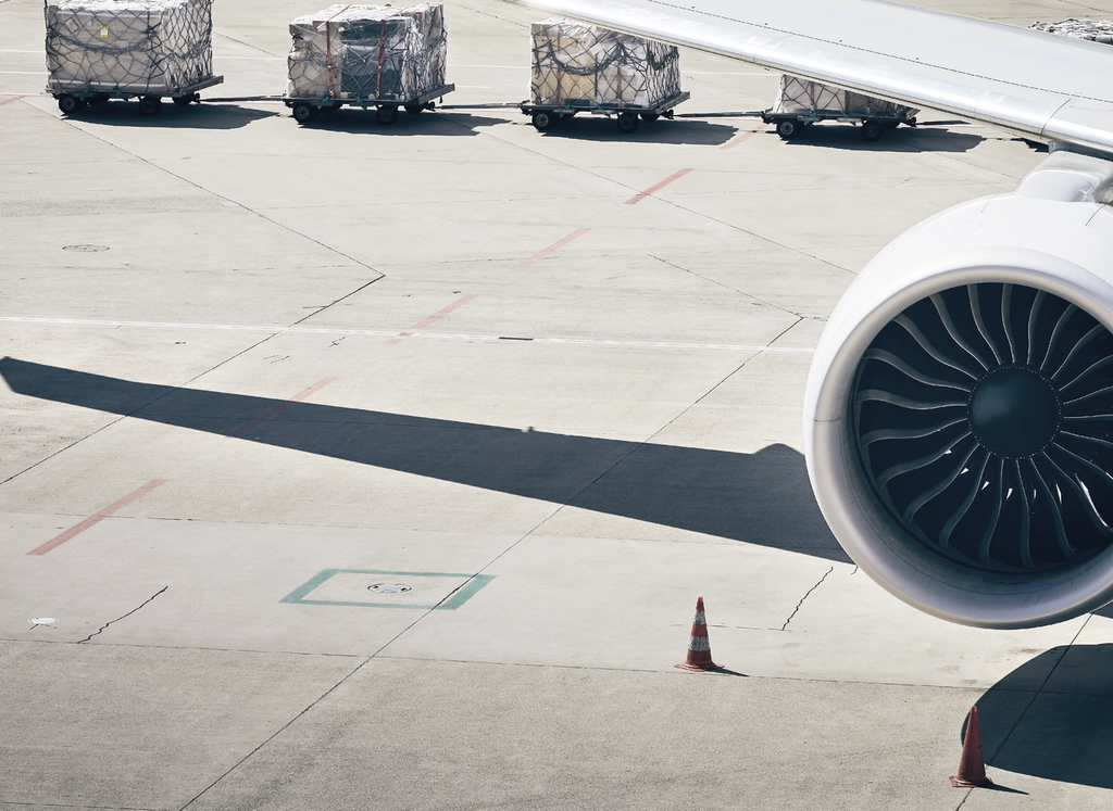 An aircraft engine and wing mounted on the tarmac beside cargo containers ready for loading.