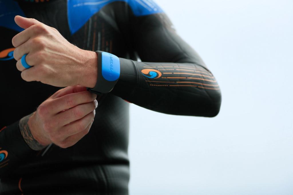 Triathlete in a wetsuit fastening a blue Sharkbanz band on the forearm