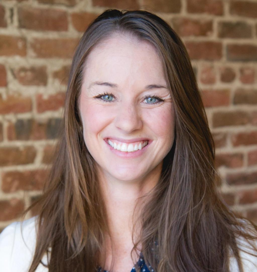 Smiling woman with long brown hair posing against an exposed red brick wall
