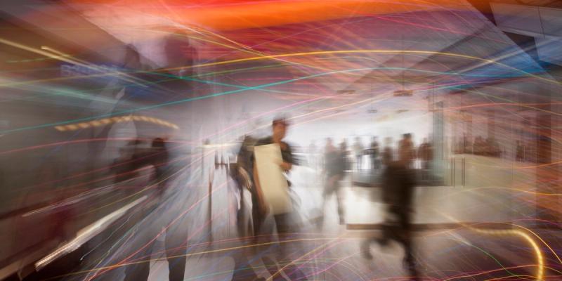 Long-exposure blur of people walking through a transit hall streaked with multicolored light trails